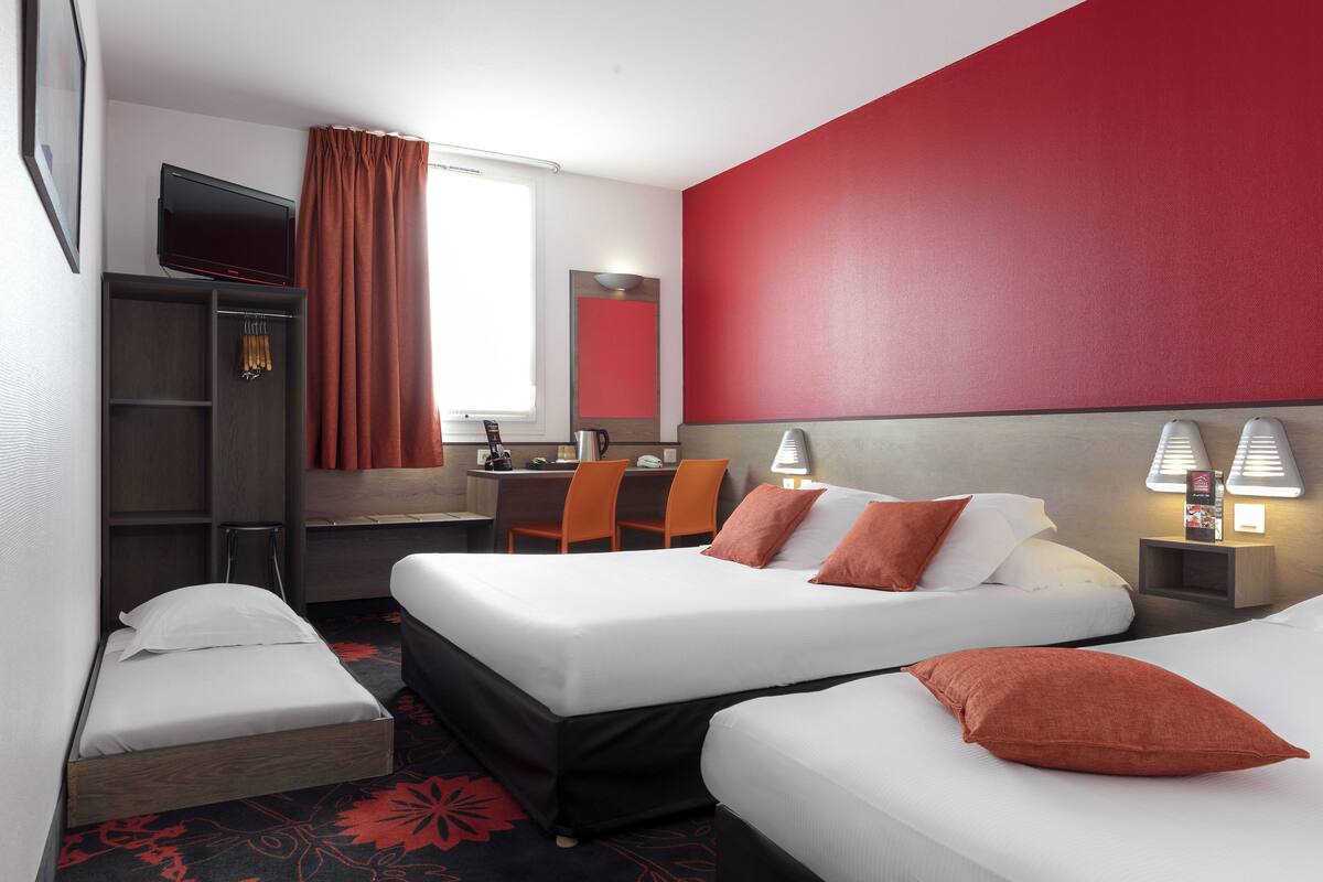 Une chambre d’hôtel avec deux lits, un bureau avec une chaise, une télévision et un mur d’accent de couleur rouge.