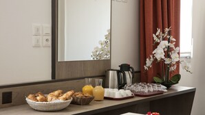 Una mesa con desayuno que incluye croissants, zumo de naranja, una cafetera y un jarrón con flores.