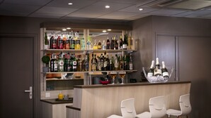 Zona de bar con varias estanterías llenas de botellas, una vitrina de cristal y tres taburetes blancos.