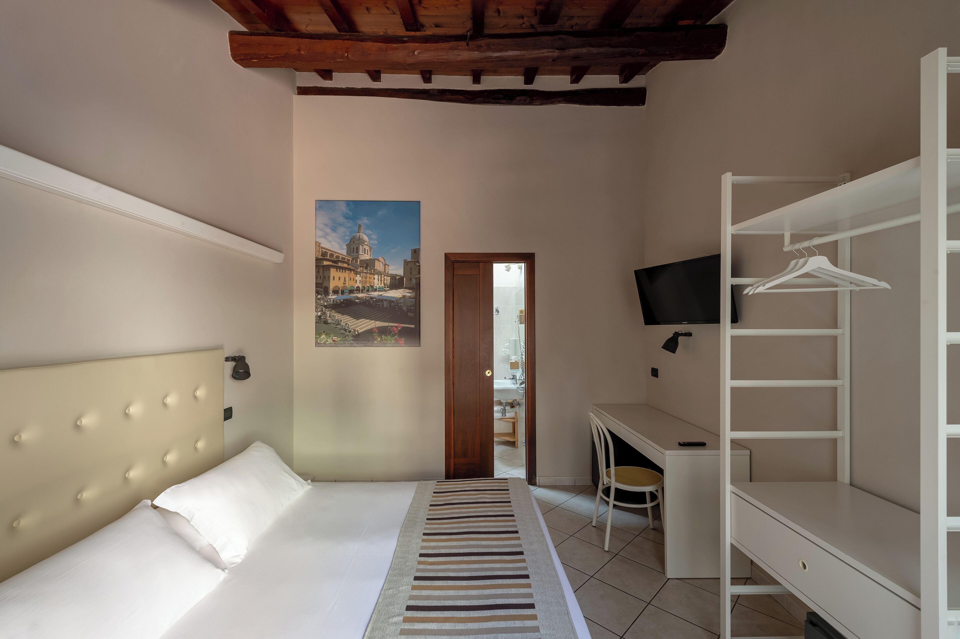 A hotel room with a bed, a desk, a chair, a TV, and a wardrobe.