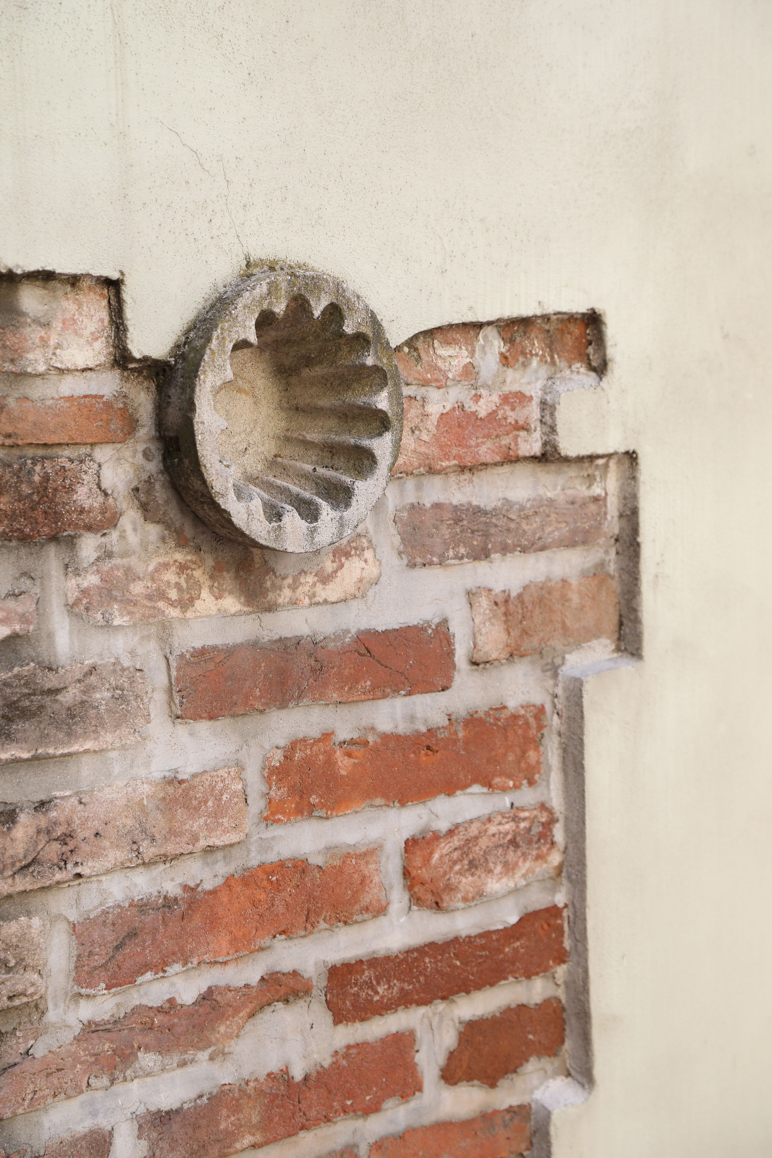 Een bakstenen muur met een rond, verweerd metalen object erin.