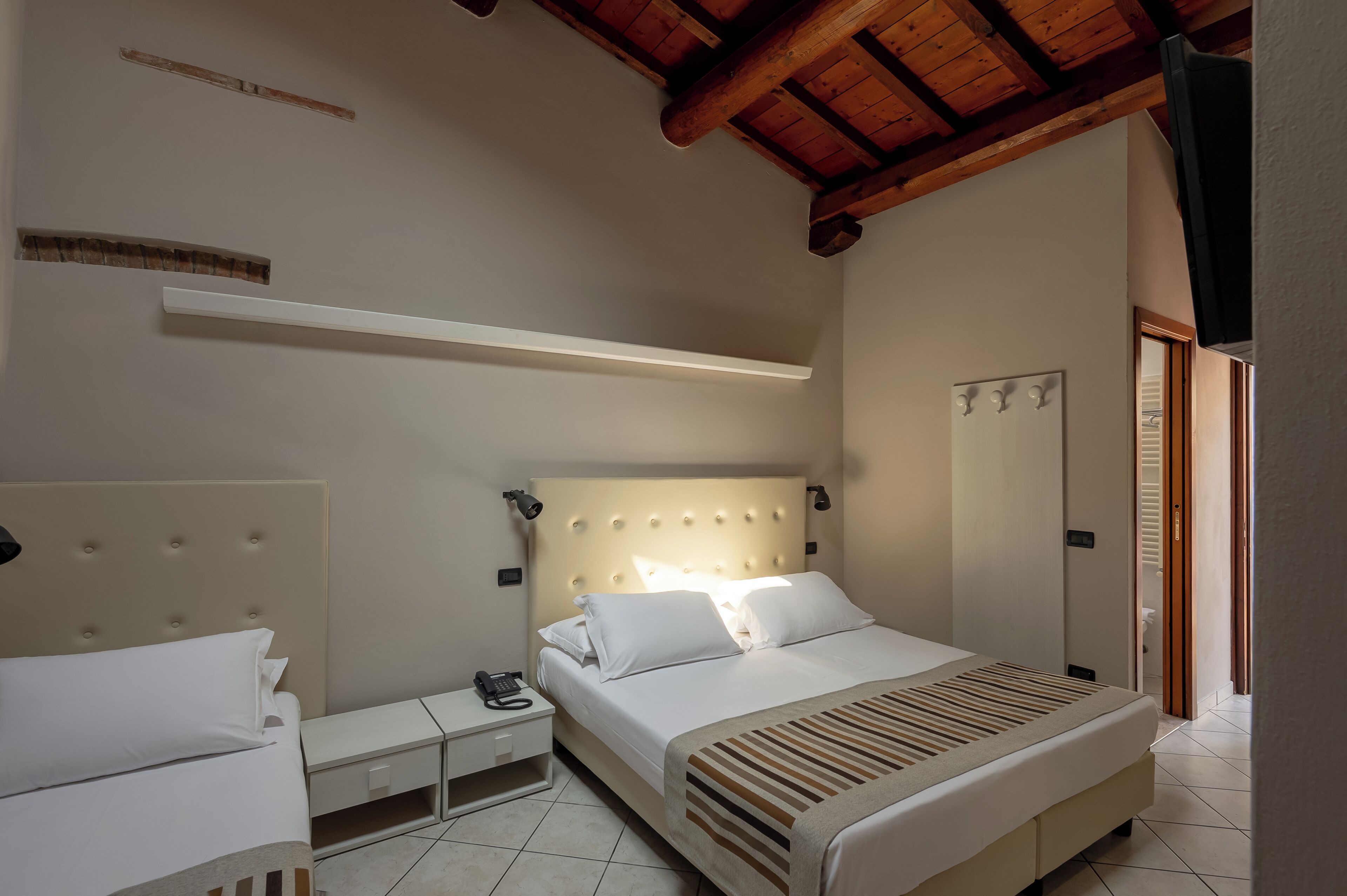Ein Schlafzimmer mit einem Bett, Nachttischen, einem Telefon, einem Spiegel und einer Decke mit Holzbalken.