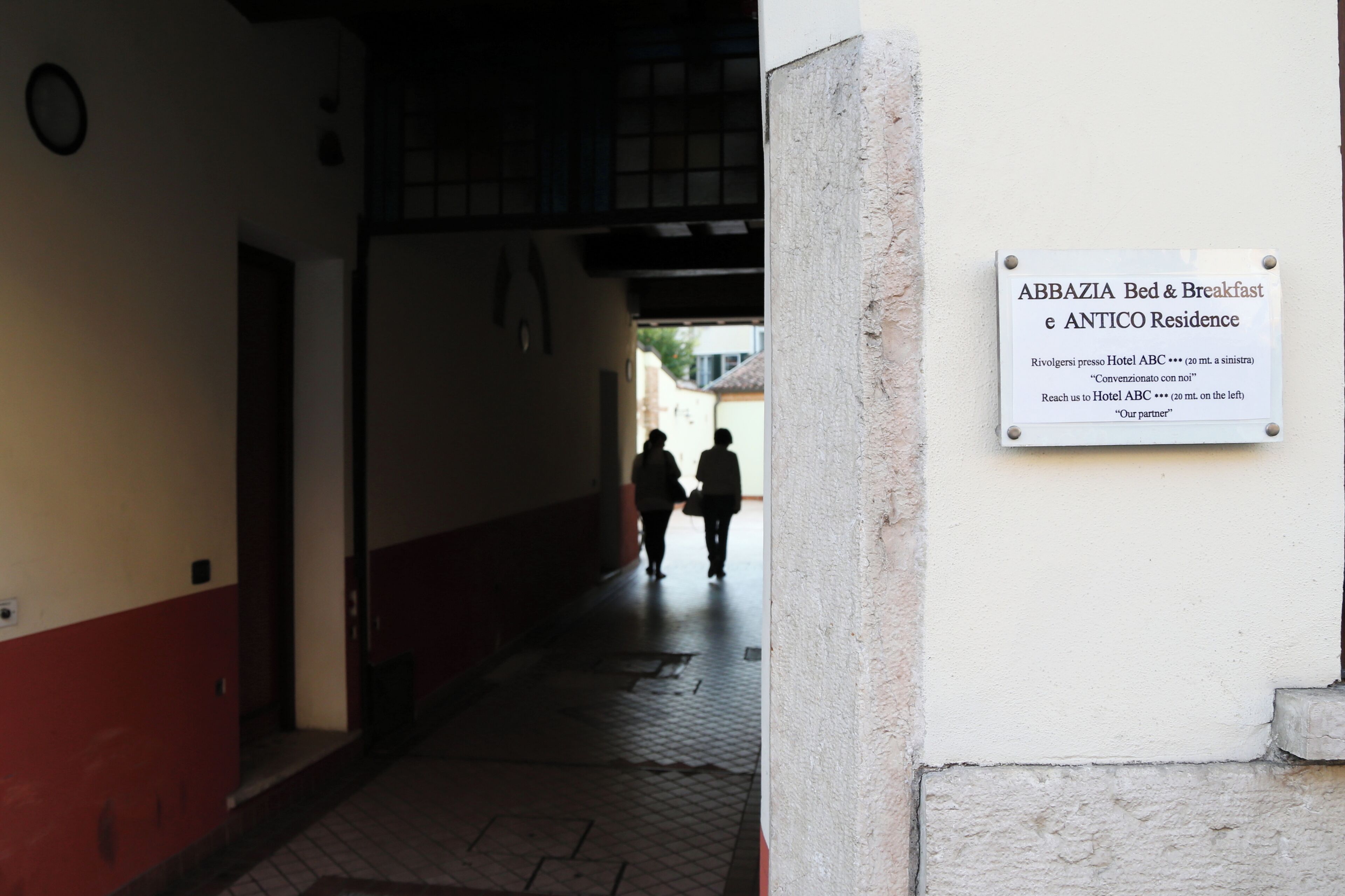 A narrow corridor with a sign indicating 'ABBAZIA Bed & Breakfast e ANTICO Residence' and directions to Hotel ABC.