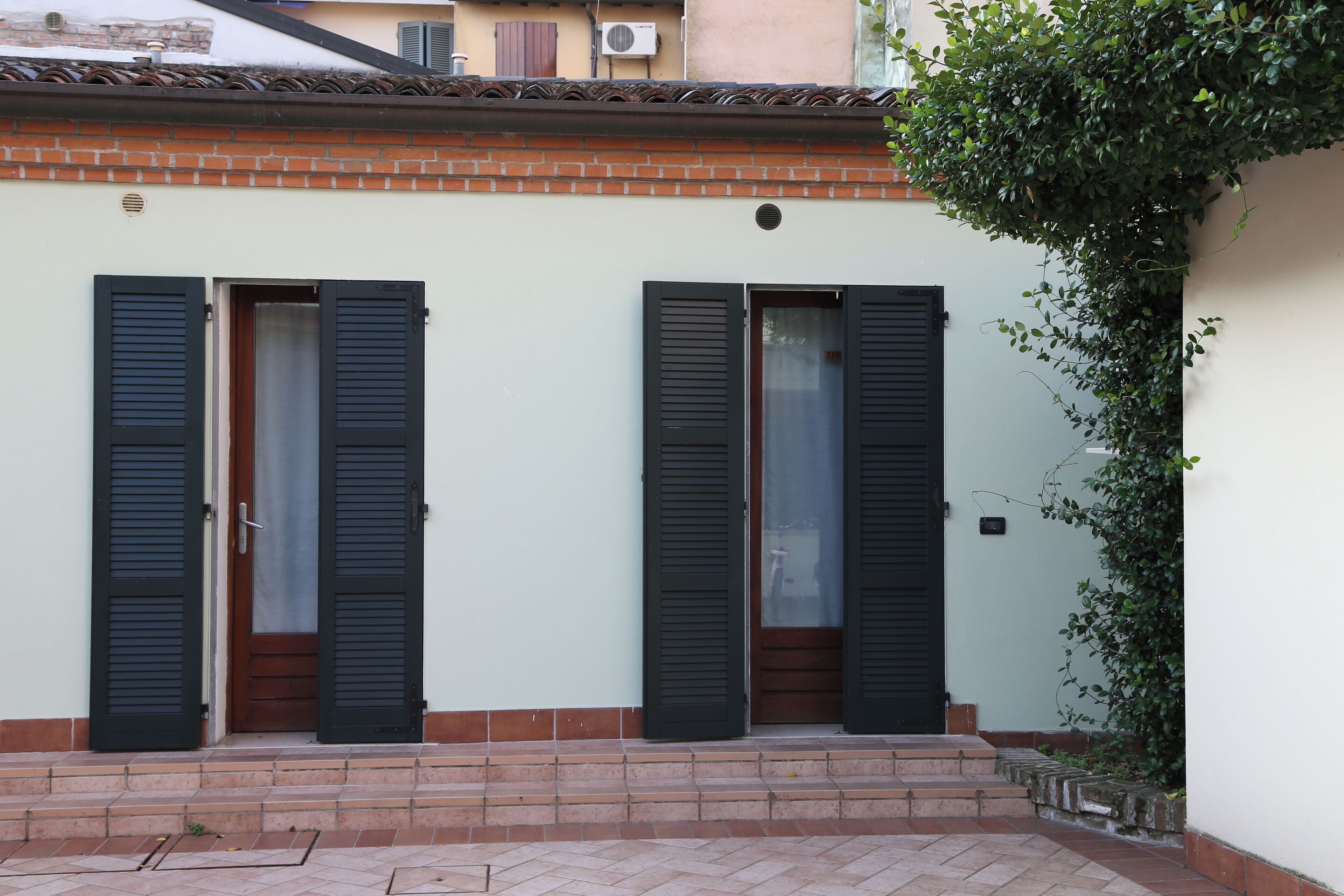 A building with two doors, each with a wooden door and black shutters, and a brick base.