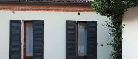 Un edificio con dos puertas, cada una con una puerta de madera y contraventanas negras, y una base de ladrillo.