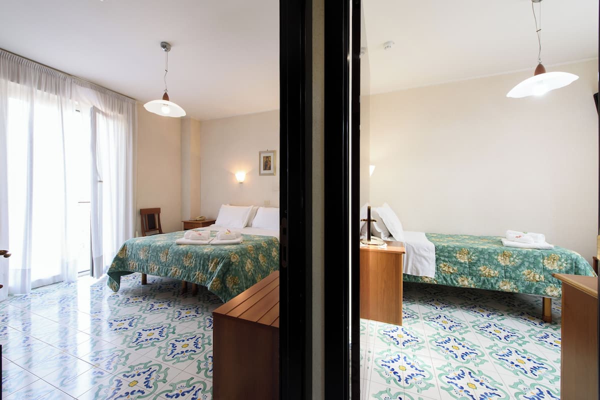 Habitación de hotel con dos camas, un banco de madera, una mesita pequeña y una mesita de noche.