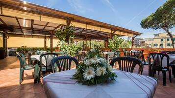 Een terras met tafels en stoelen, een overdekte zithoek en uitzicht op de omliggende gebouwen.