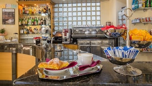 Een bar met een koffieapparaat, een gebakje, en een schaal met een kop koffie en een croissant.
