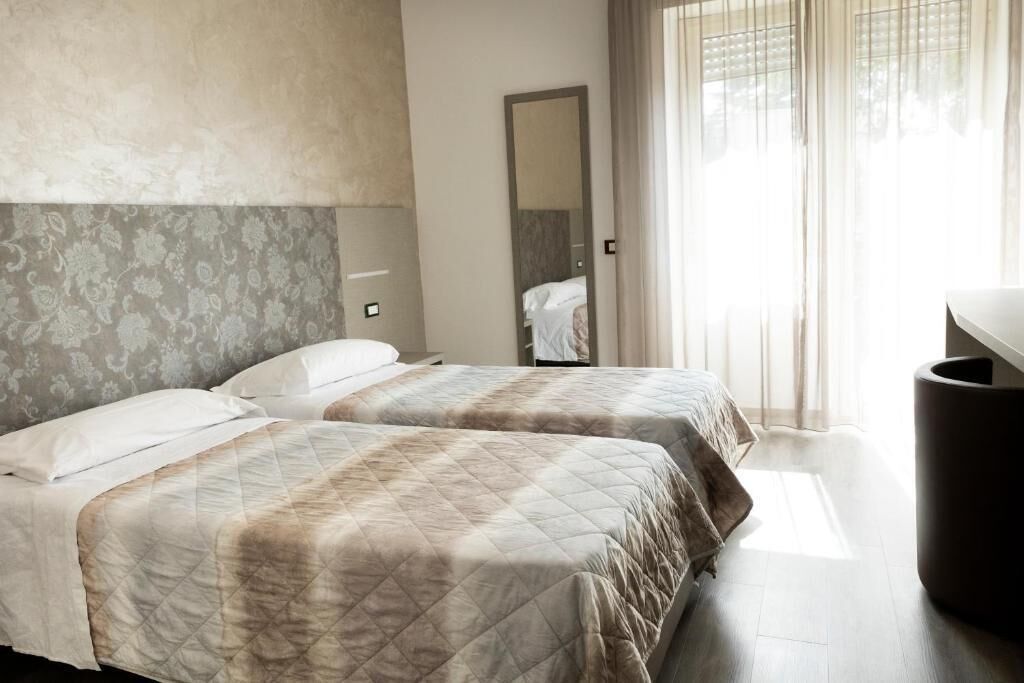 A hotel room with two beds, a large mirror, and a window with curtains.
