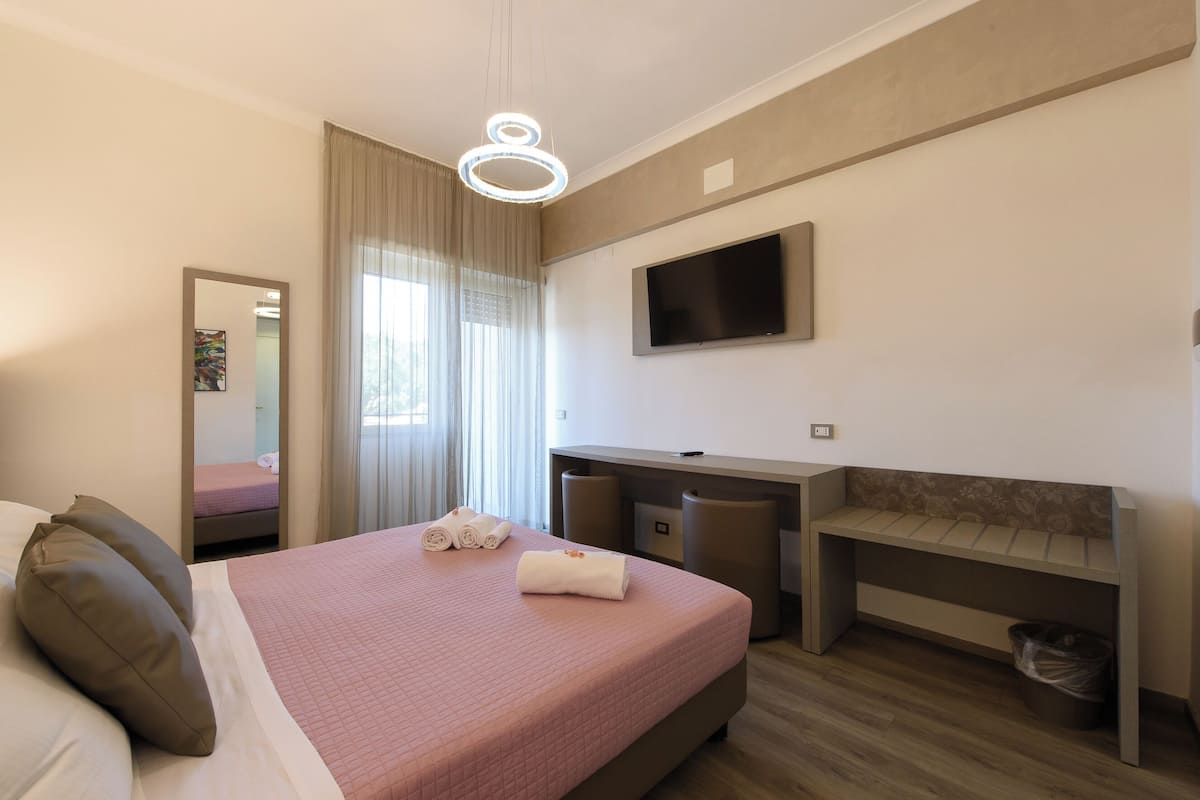 Una habitación de hotel con cama, escritorio, televisor y espejo.
