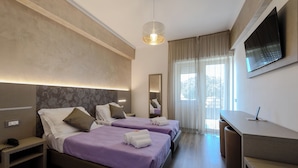 Een hotelkamer met twee bedden, een bureau, een televisie en een groot raam met gordijnen.