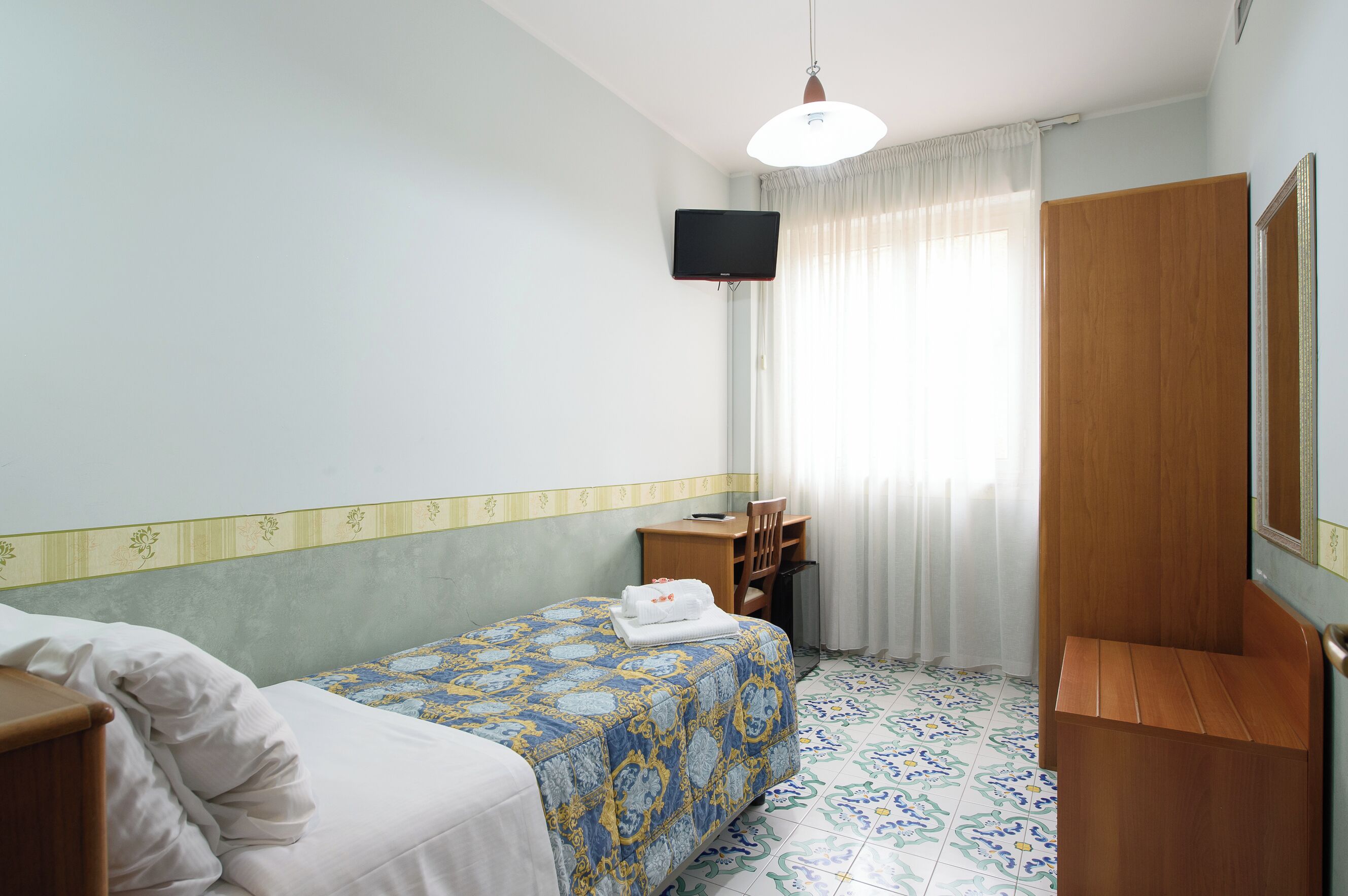 Une chambre d’hôtel équipée d’un lit, d’un bureau, d’une chaise, d’une télévision et d’une armoire.