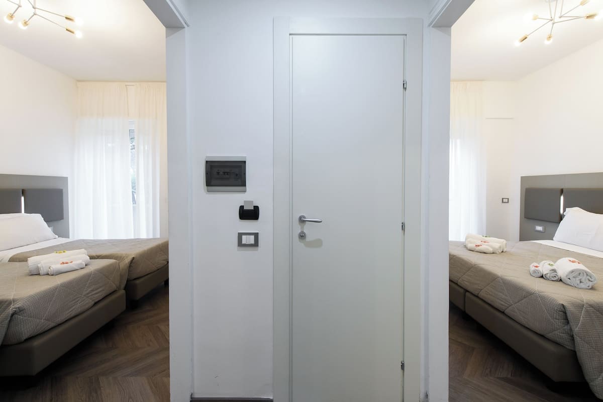 Habitación de hotel con dos camas, una puerta blanca, un interruptor de luz y un enchufe en la pared.
