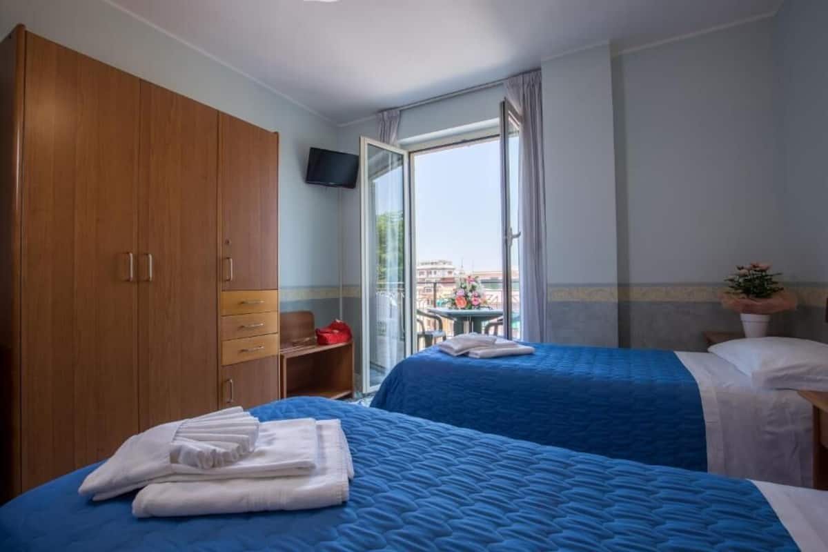 Habitación de hotel con dos camas, un armario de madera, televisión y vista de la ciudad a través de un ventanal.