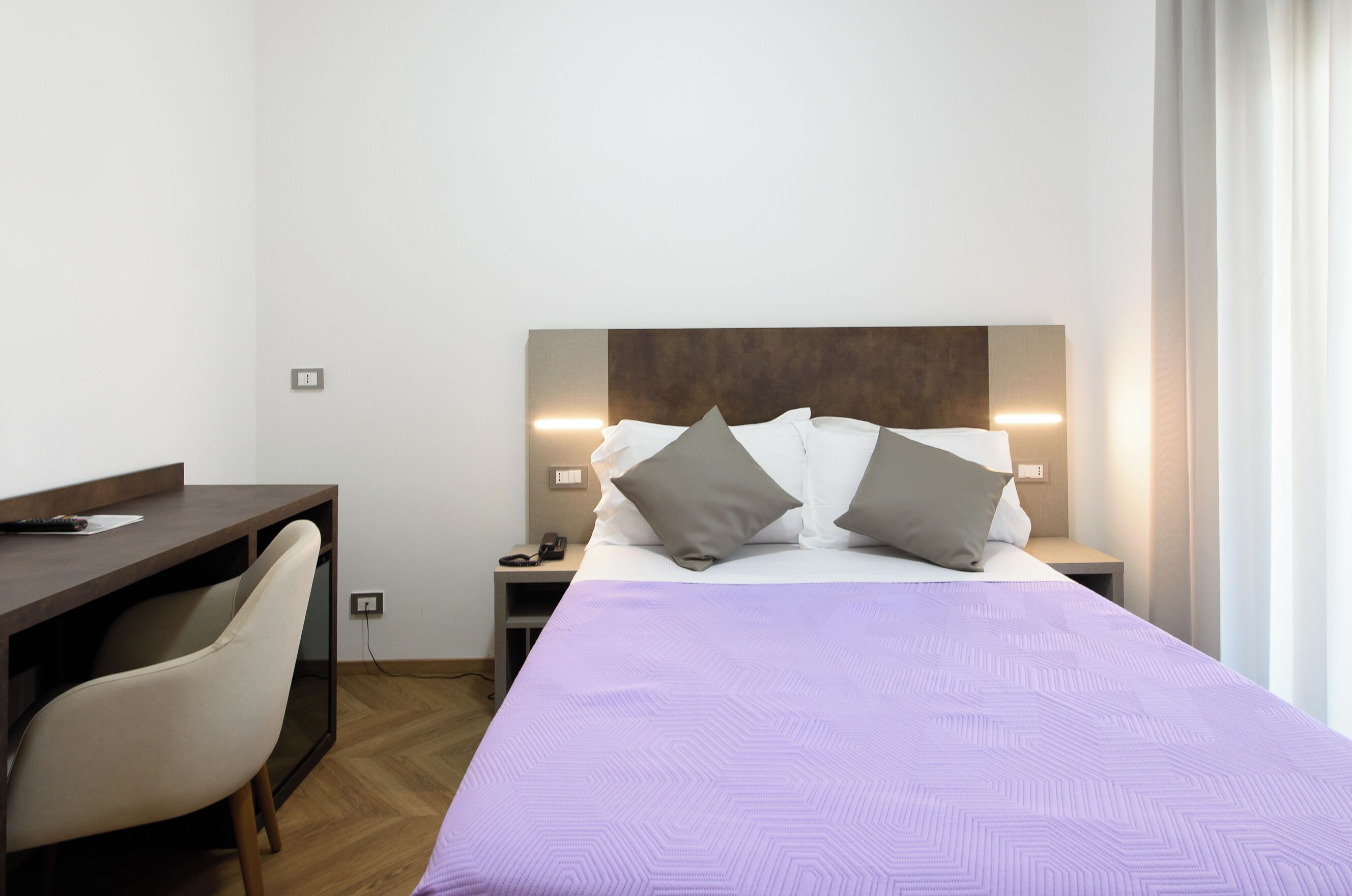 A hotel room with a bed, a desk, and a chair. There are two bedside tables with lamps.
