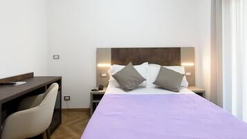 A hotel room with a bed, a desk, and a chair. There are two bedside tables with lamps.