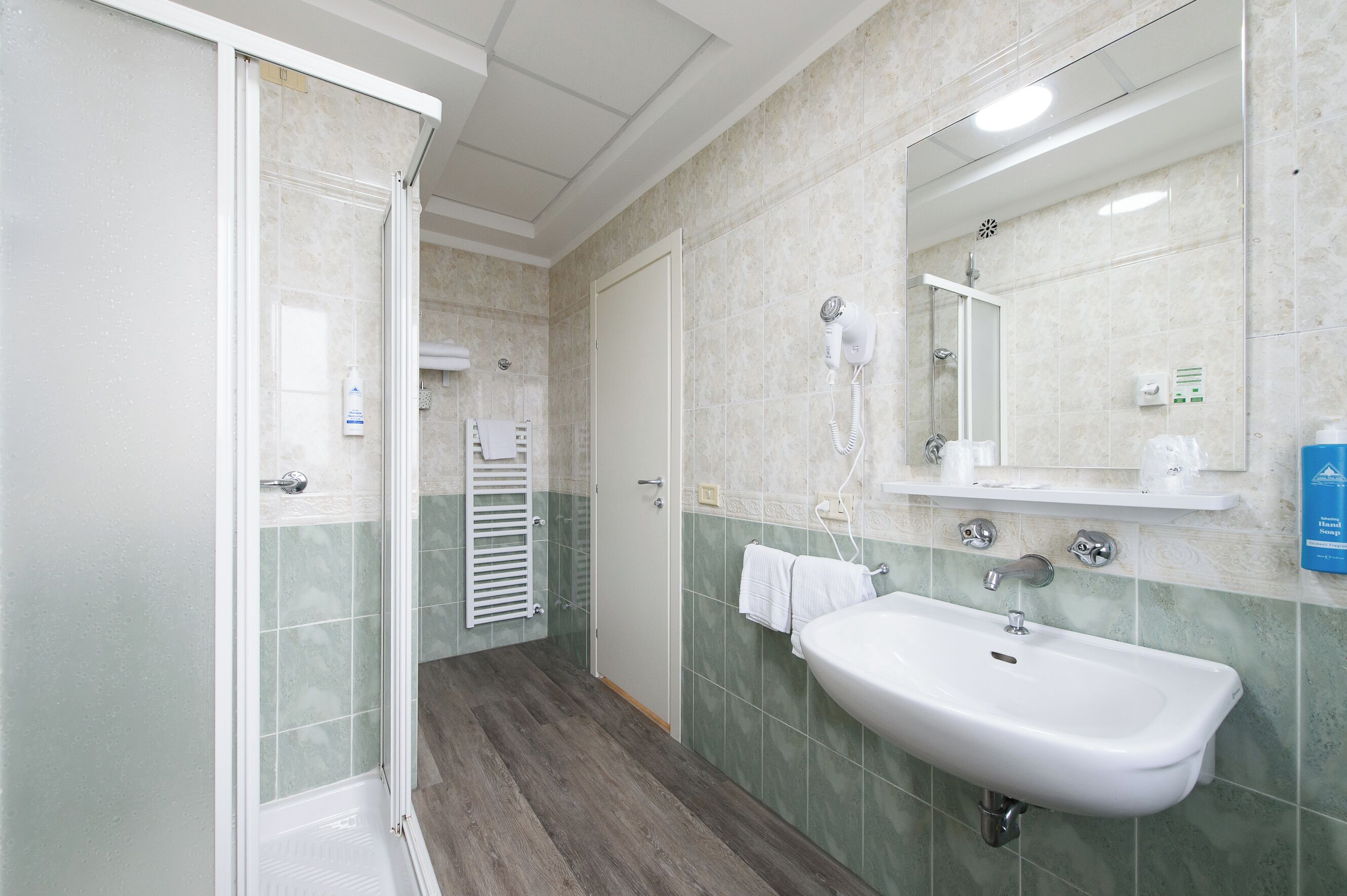 A bathroom with a shower, a sink, a mirror, and a towel rack.