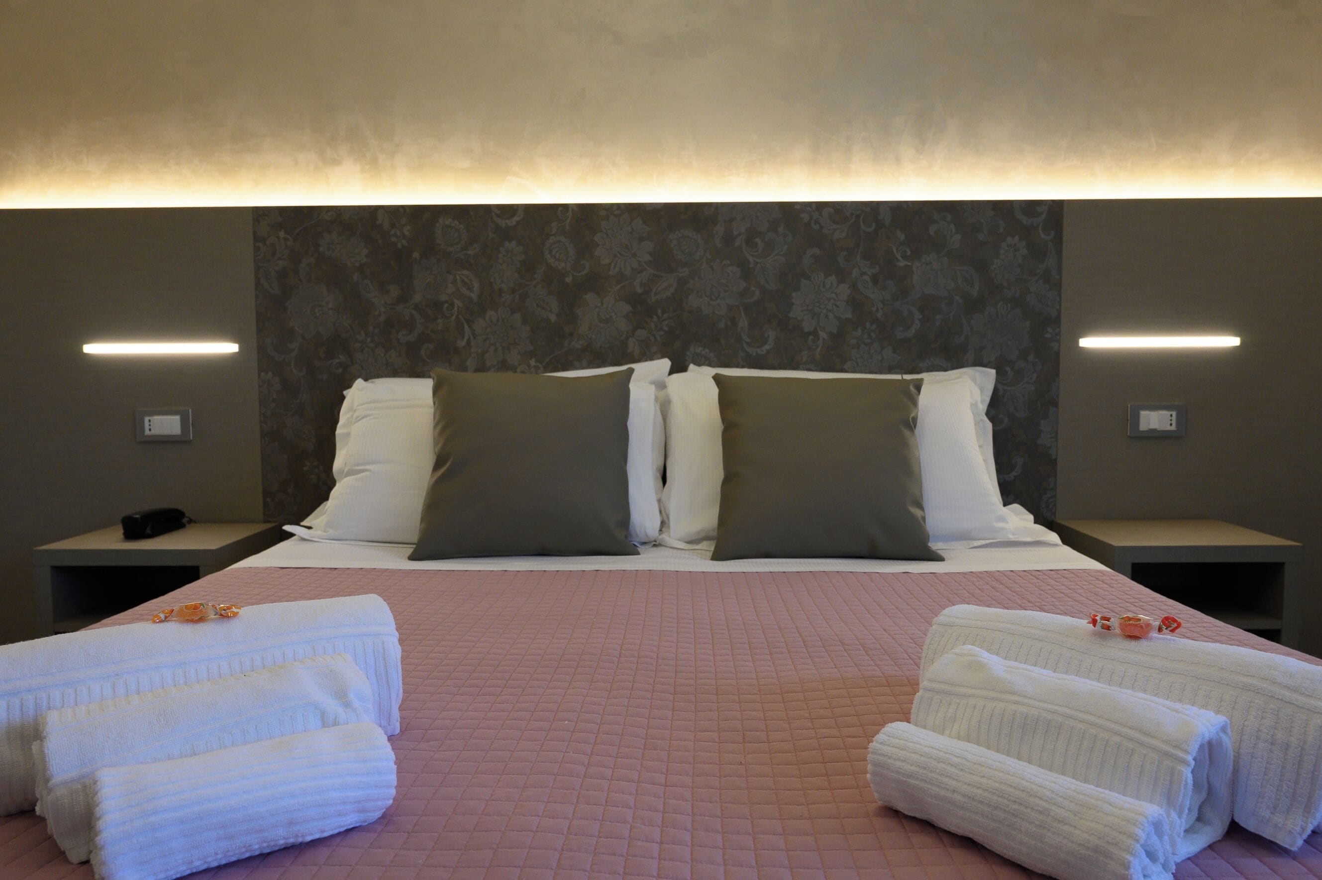 A hotel room with a large bed, two bedside tables, and a headboard with a floral pattern.