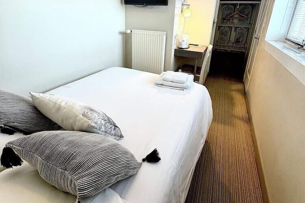 Habitación de hotel con cama, televisor, radiador, una mesita con lámpara y armario.