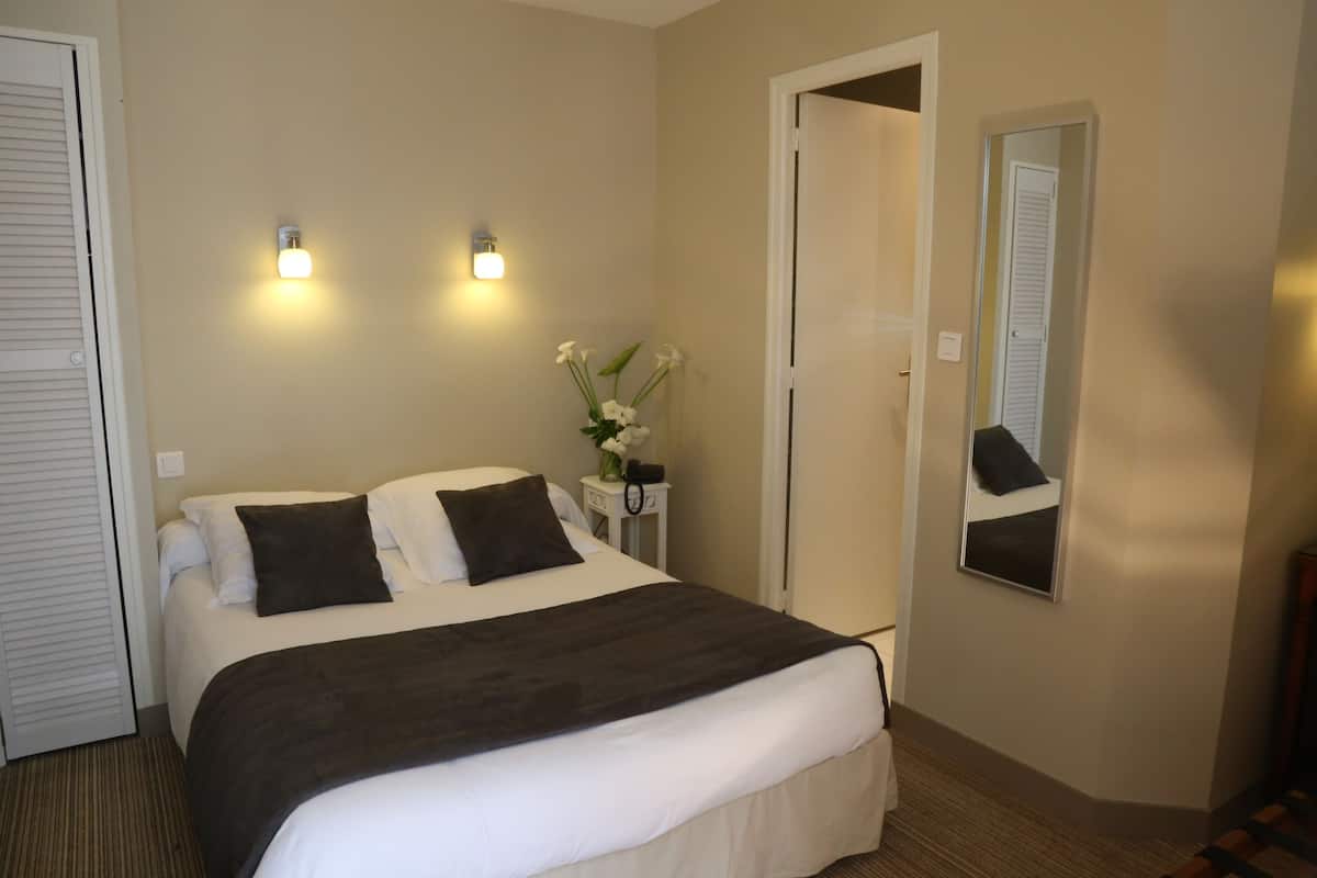Una habitación de hotel con cama, lámparas de noche, espejo y una puerta.