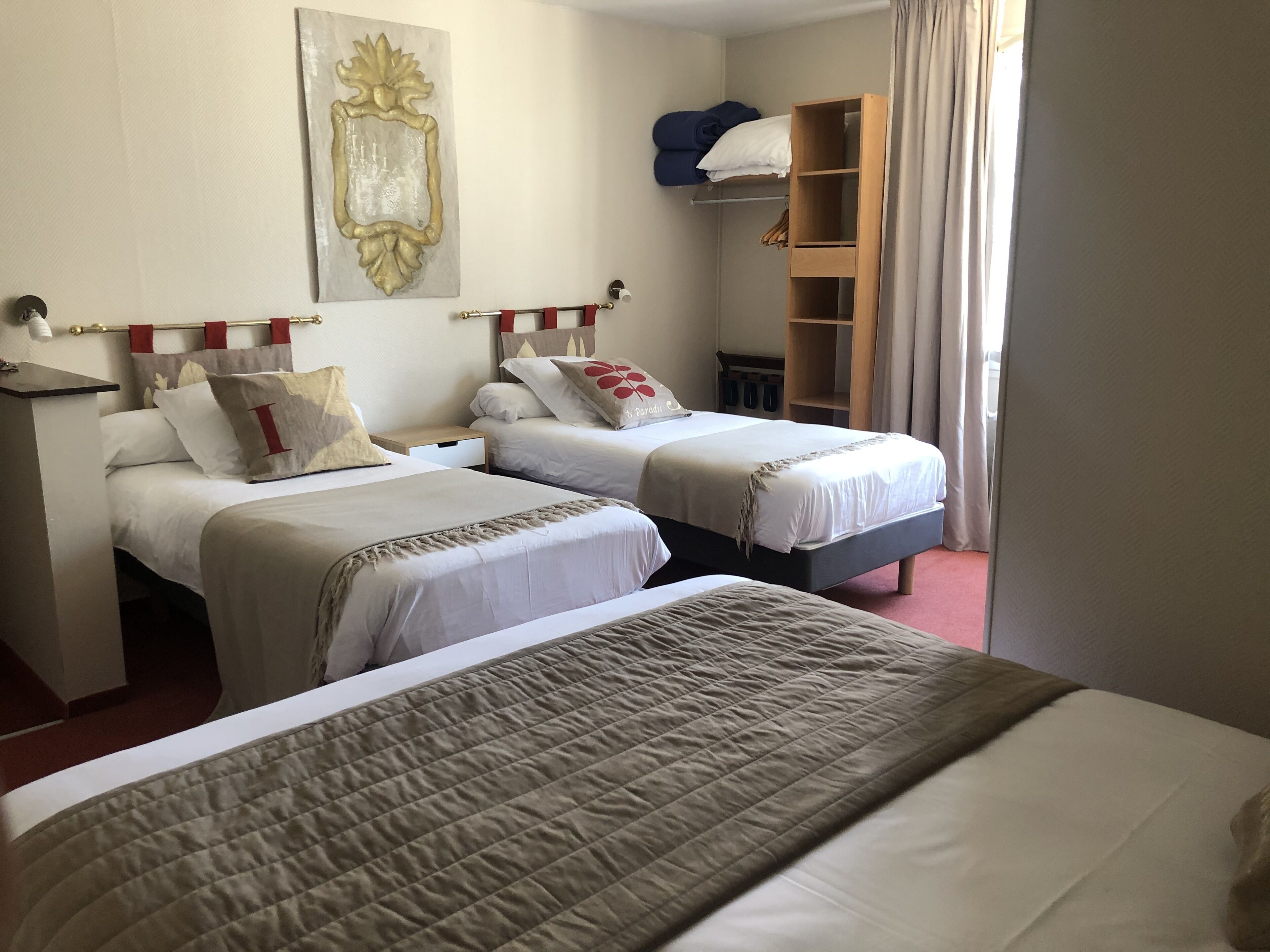 A hotel room with two beds, a wardrobe, a mirror, and a painting on the wall.