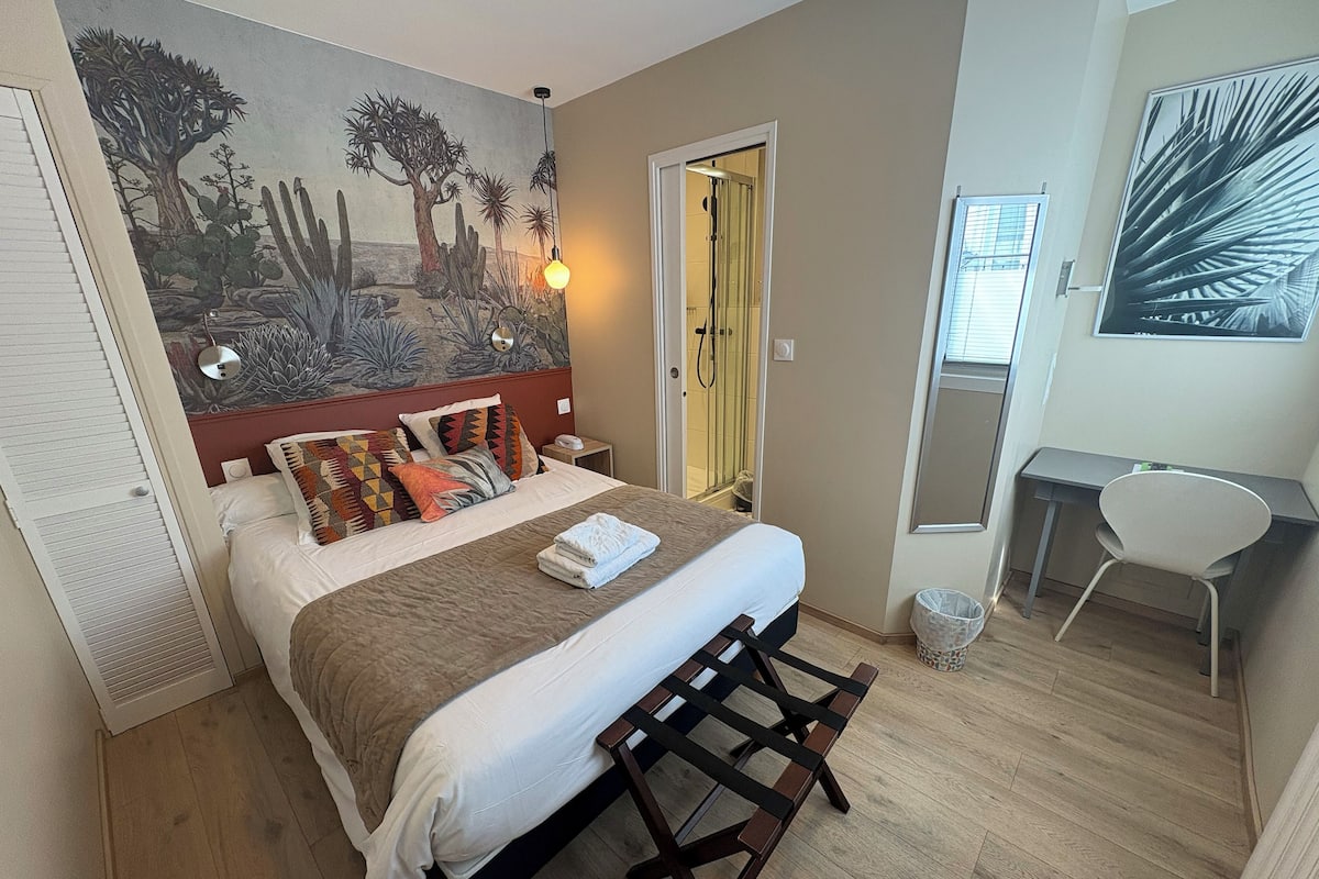 Un dormitorio con cama, escritorio, silla, ducha y un mural en la pared.