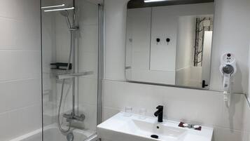 Ett modernt badrum med en dusch som är avskärmad med glasväggar, ett vitt handfat och en hårtork som är monterad på väggen.