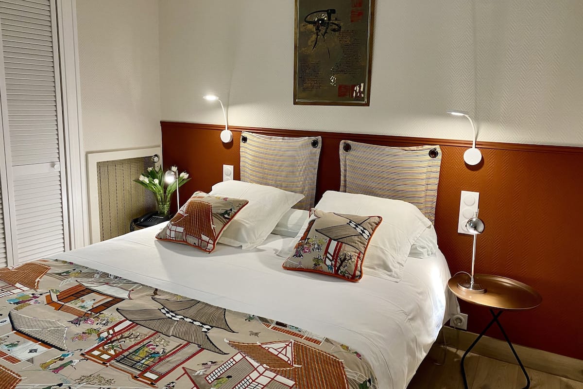 Habitación de hotel con cama, dos lámparas de noche, un cuadro en la pared y un tapete decorativo.