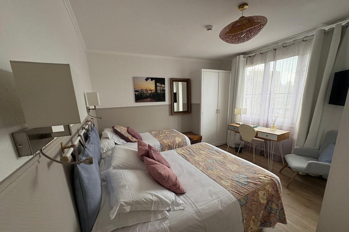 Habitación de hotel con dos camas, un escritorio, una silla, un televisor y una ventana con cortinas.