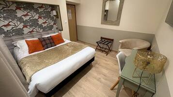 Hotellihuone, jossa on sänky, kirjoituspöytä lampun kanssa, tuoli ja peili seinällä.
