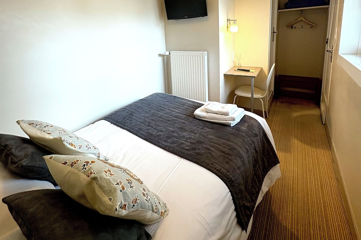 Habitación de hotel con cama, televisor de pantalla plana montado en la pared, escritorio con silla y vestidor.