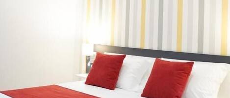 A hotel room with a bed, a striped wall, and a red and white bedspread.