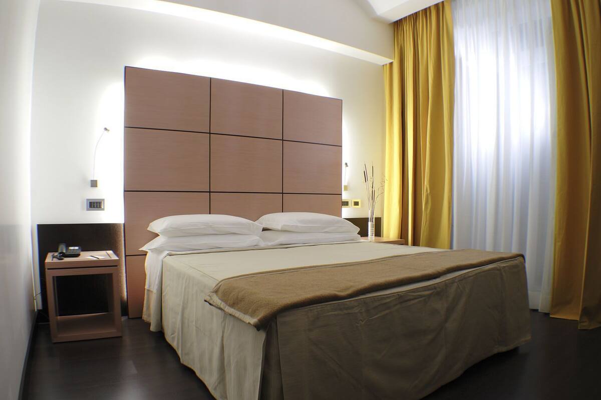 A hotel room with a large bed, a bedside table with a phone, and a nightstand.