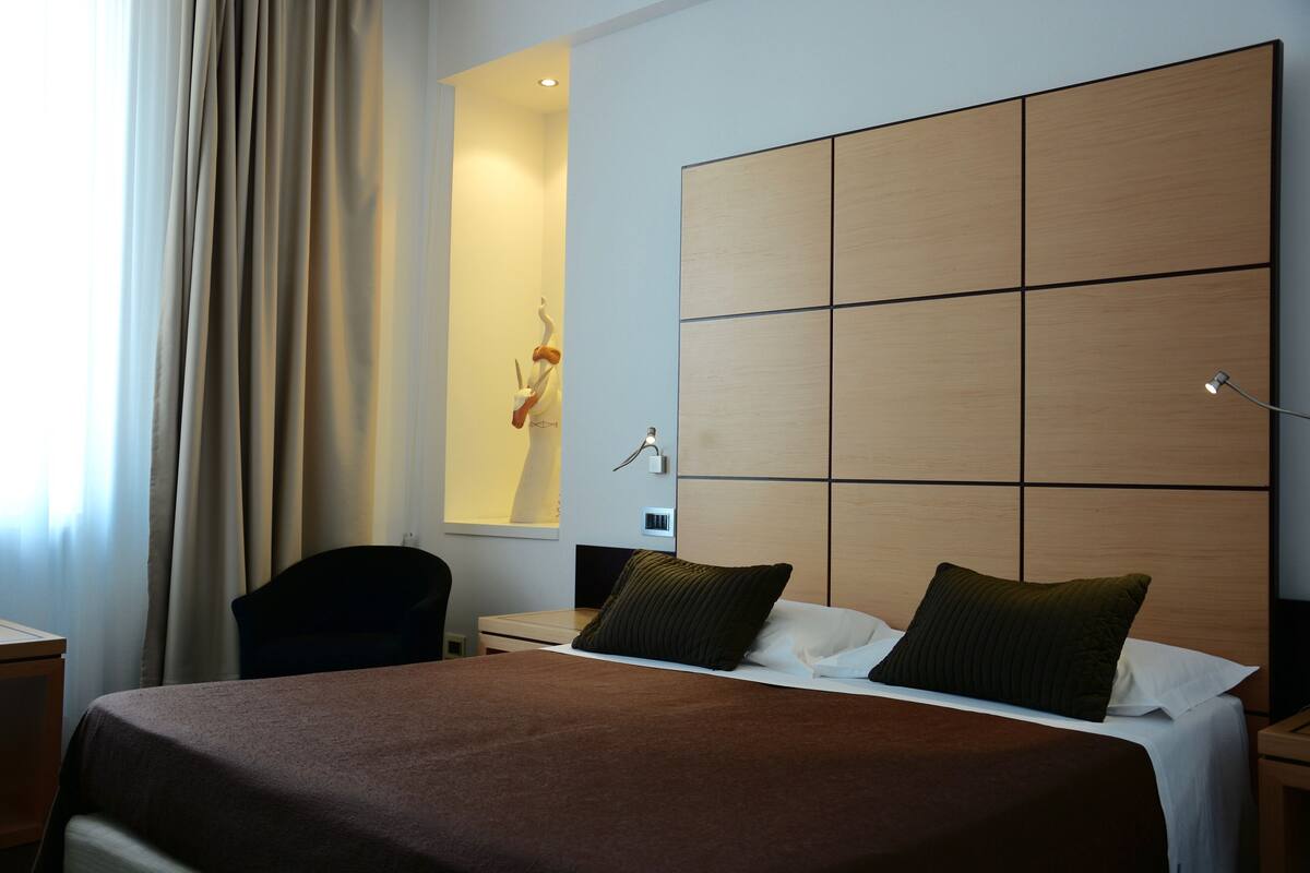 A hotel room with a large bed, a desk, a chair, and a mirror.