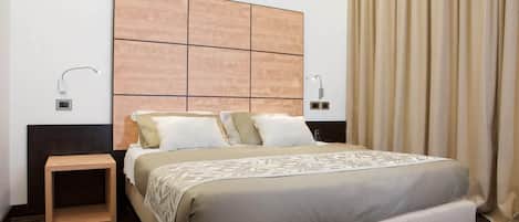 A modern hotel room with a large bed, a wooden headboard, bedside lamps, and a small wooden nightstand.