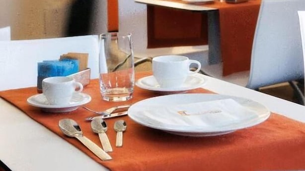 A dining area with tables set for two, each with a white tablecloth, a glass, a cup, and cutlery. - Hotel Cimarosa (Naples)