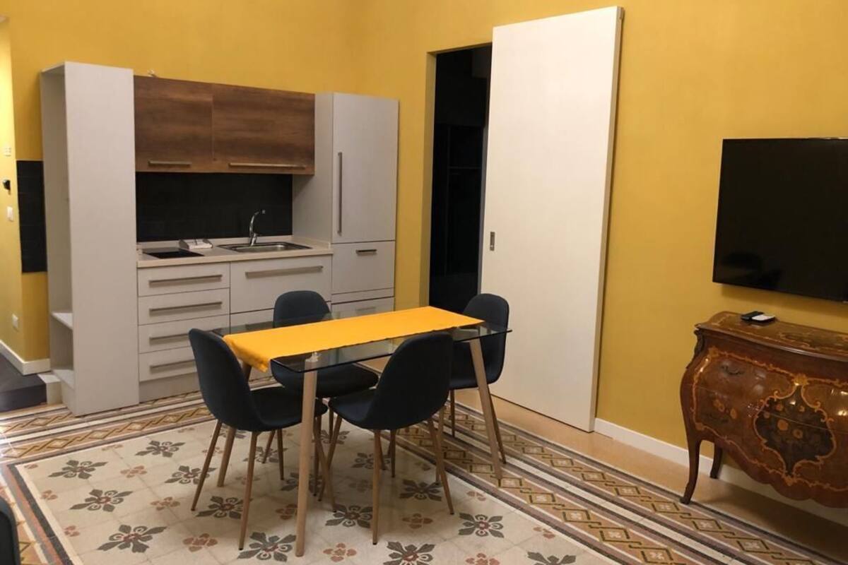 A compact kitchen with a dining table and chairs, a built-in oven, and a television on the wall.