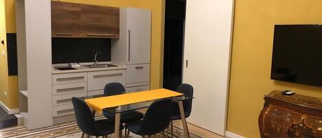 Eine kleine Küche mit Esstisch und Stühlen, einem eingebauten Backofen und einem Fernseher an der Wand.