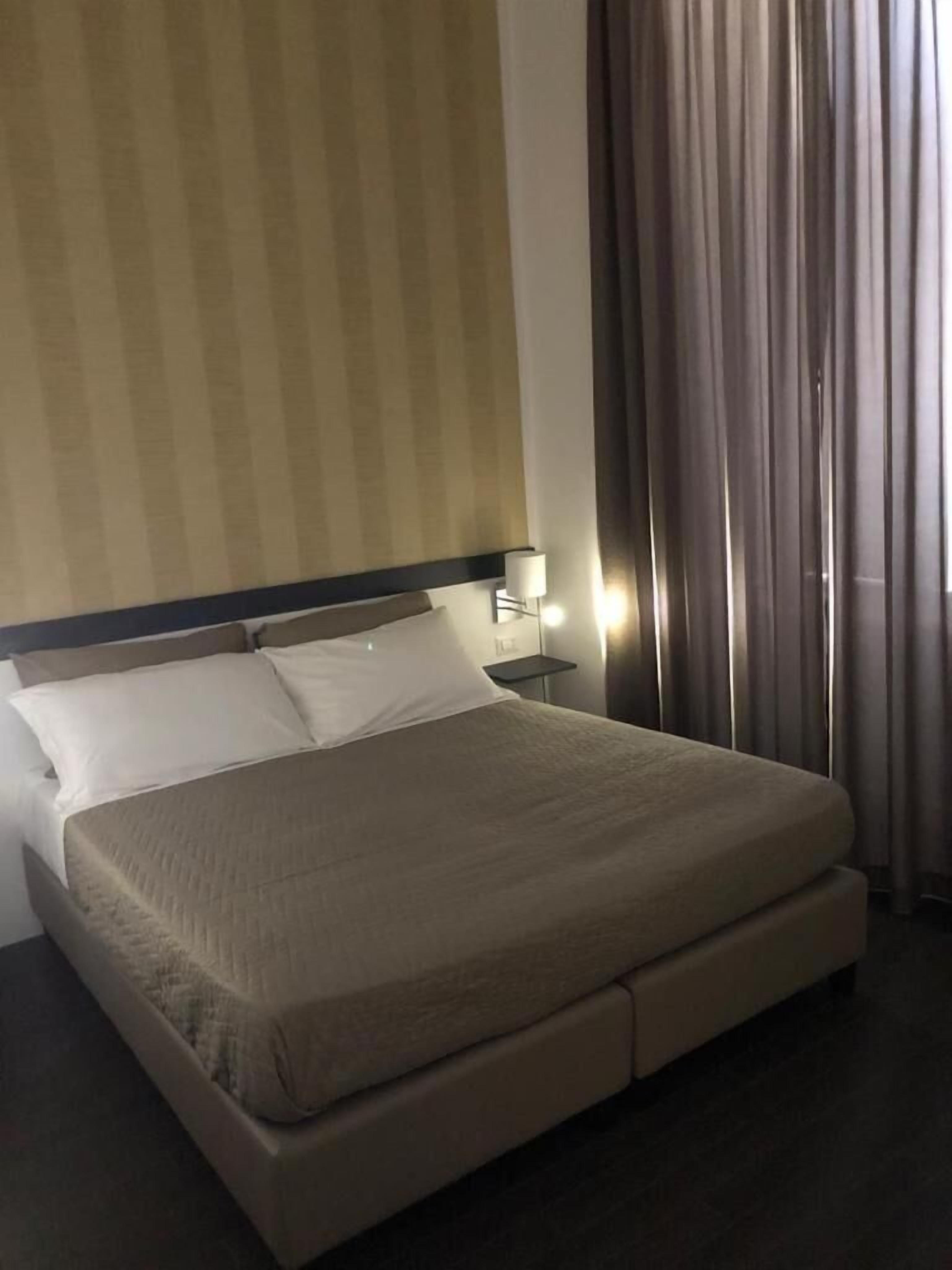A hotel room with a large bed, a nightstand, a lamp, and a window with curtains.