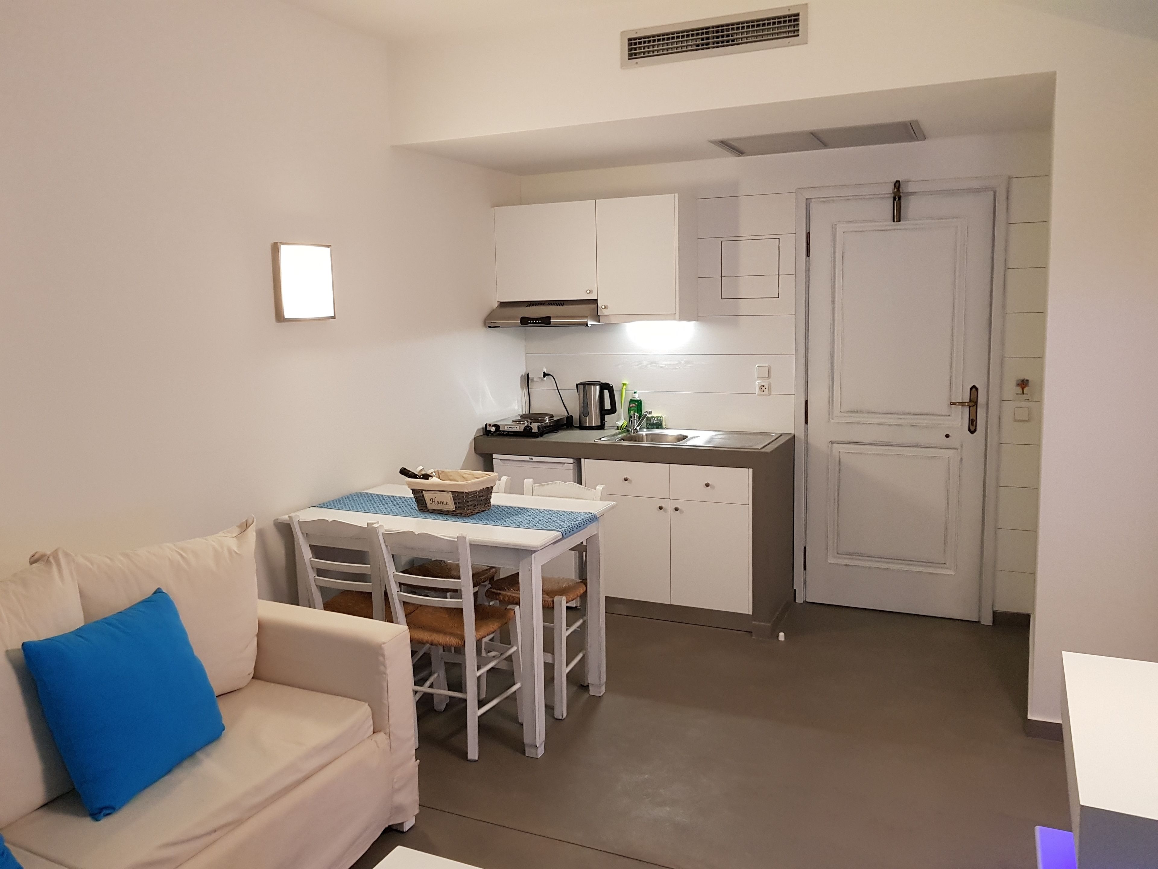 A compact living space with a kitchenette, a dining area with a table and chairs, and a sofa with a blue pillow.