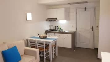 A compact living space with a kitchenette, a dining area with a table and chairs, and a sofa with a blue pillow.