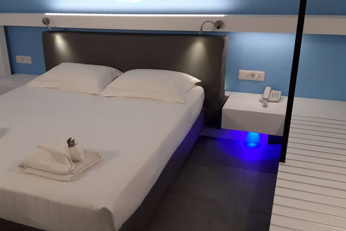 A neatly made bed with white linens and towels, a bedside phone, and a nightstand with a lamp.