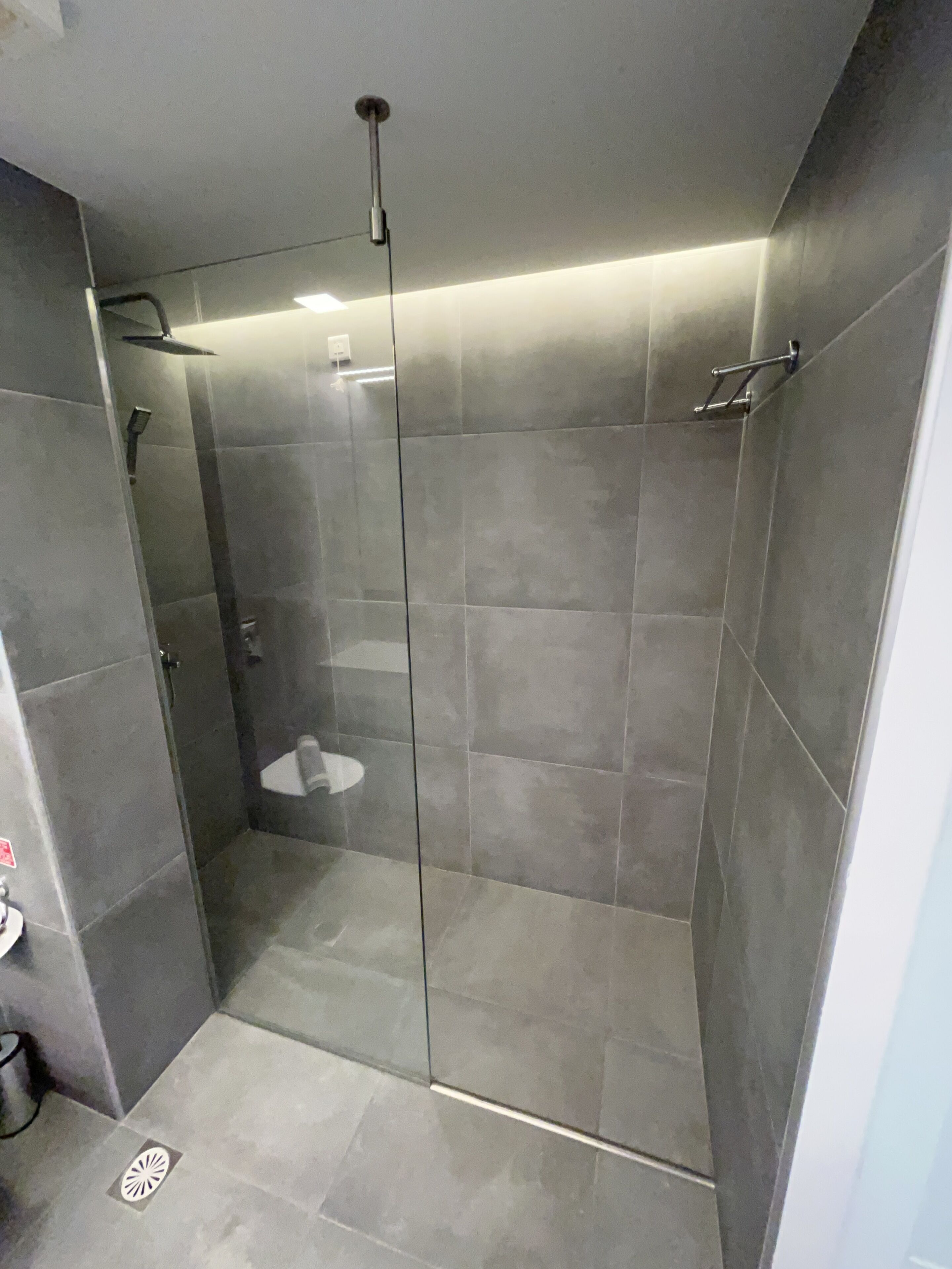 Un espace douche moderne doté d’une porte en verre, d’un pommeau de douche à main et d’un porte-serviettes fixé au mur.