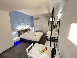 A hotel room with a bed, bedside table, and a small dining area with a table and chairs. - Niriides Hotel Apartments Studios (Apokoronas)