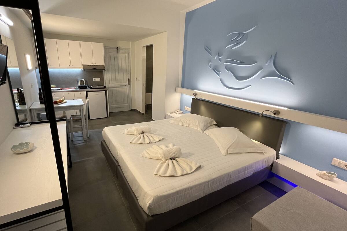 A modern hotel room with a bed, a desk, and a kitchenette.