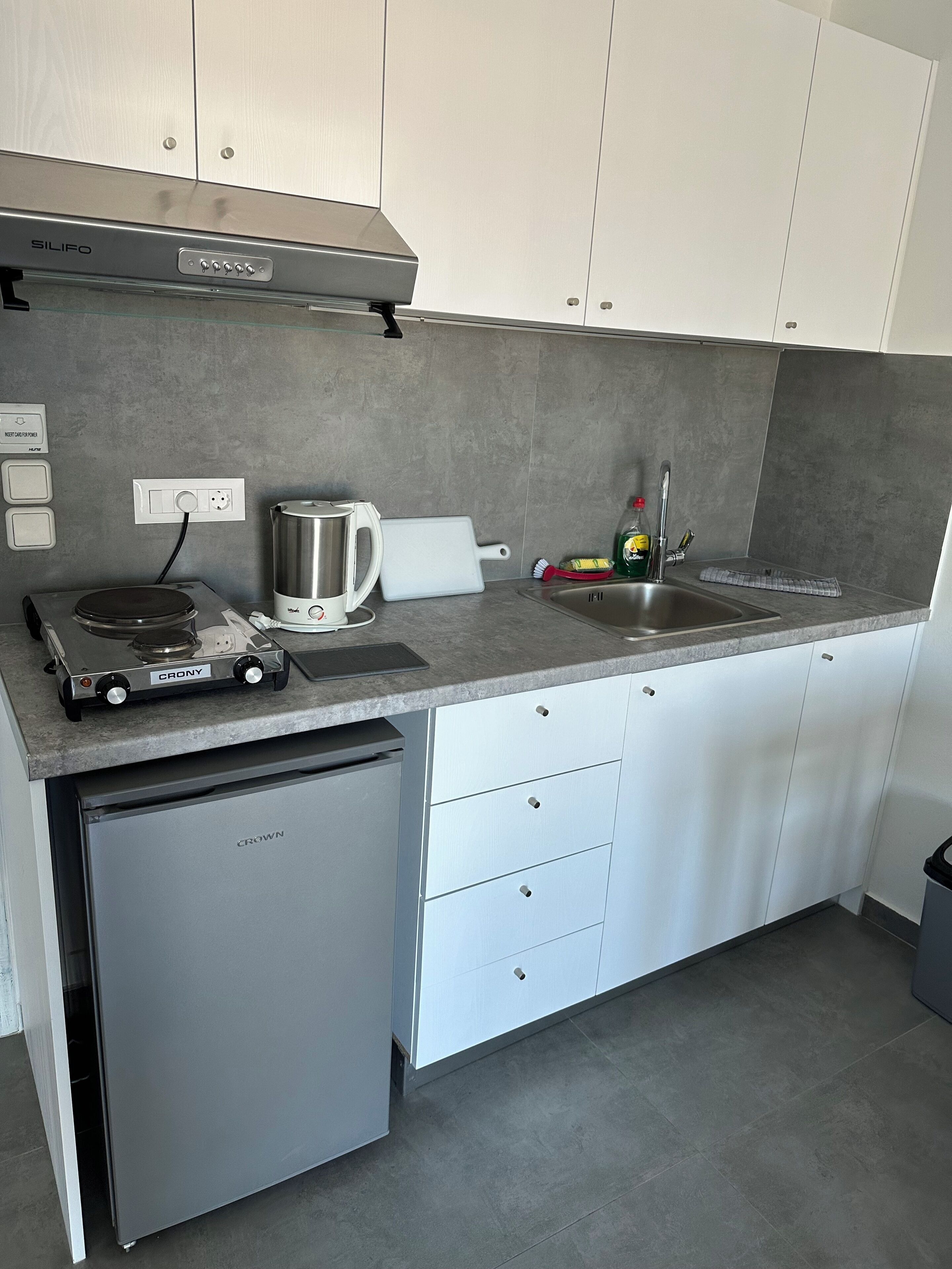 Una cocina compacta con estufa a gas, cafetera, lavavajillas y pileta.