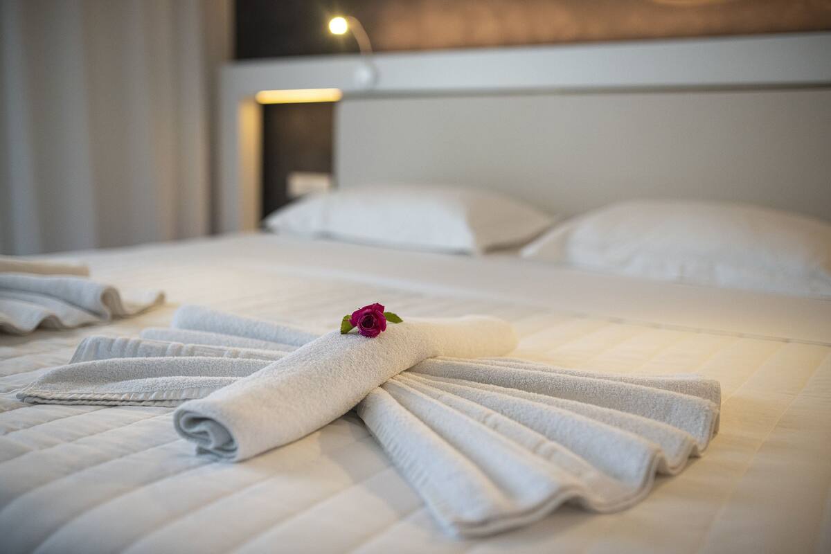 A neatly made bed with folded towels and a rose, a bedside lamp, and a headboard.
