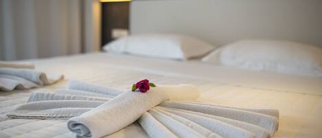 A neatly made bed with folded towels and a rose, a bedside lamp, and a headboard.