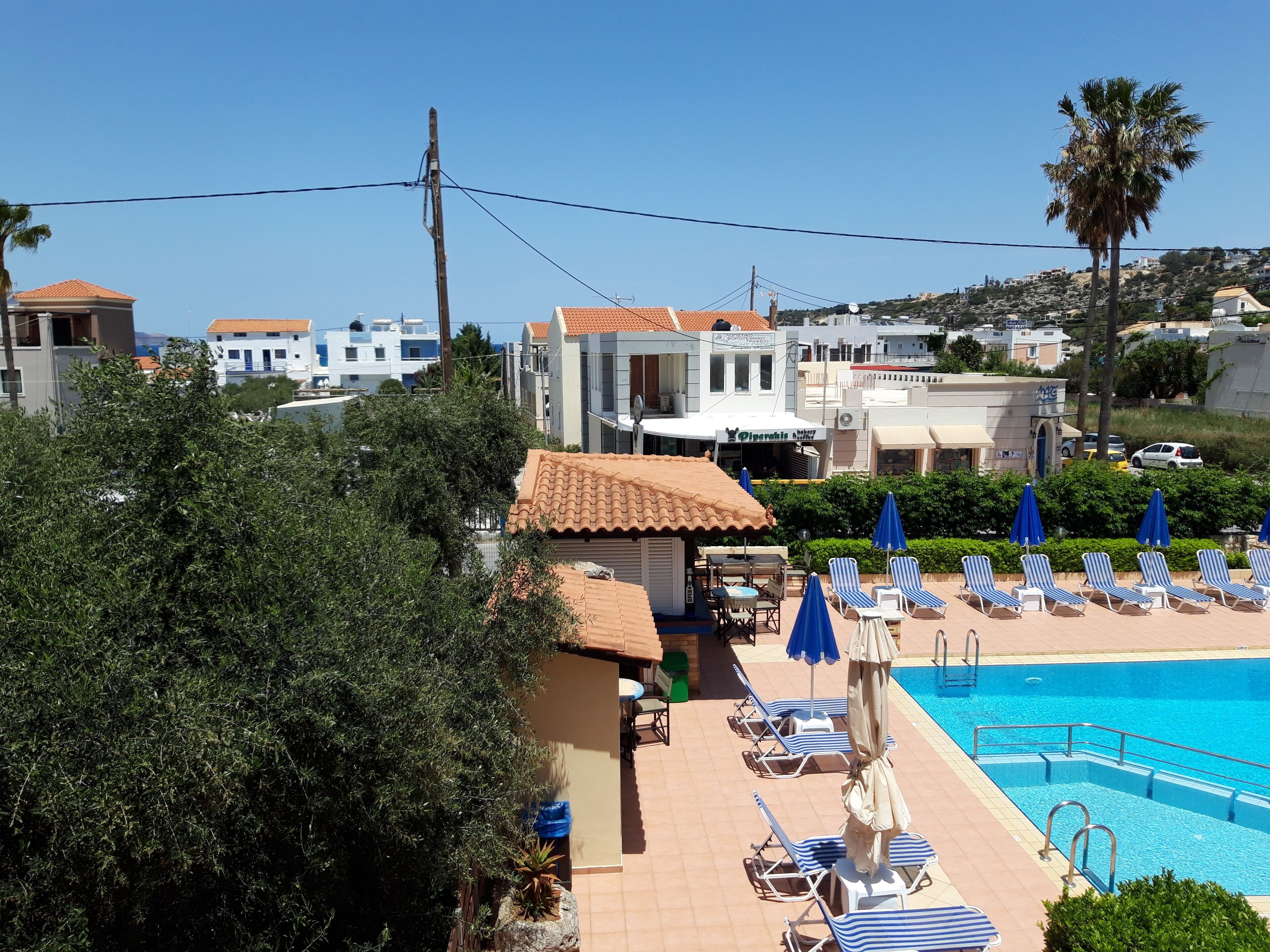 Un espace piscine avec des chaises longues et des parasols, un bâtiment doté d’un toit en tuiles et un ciel d’un bleu limpide.