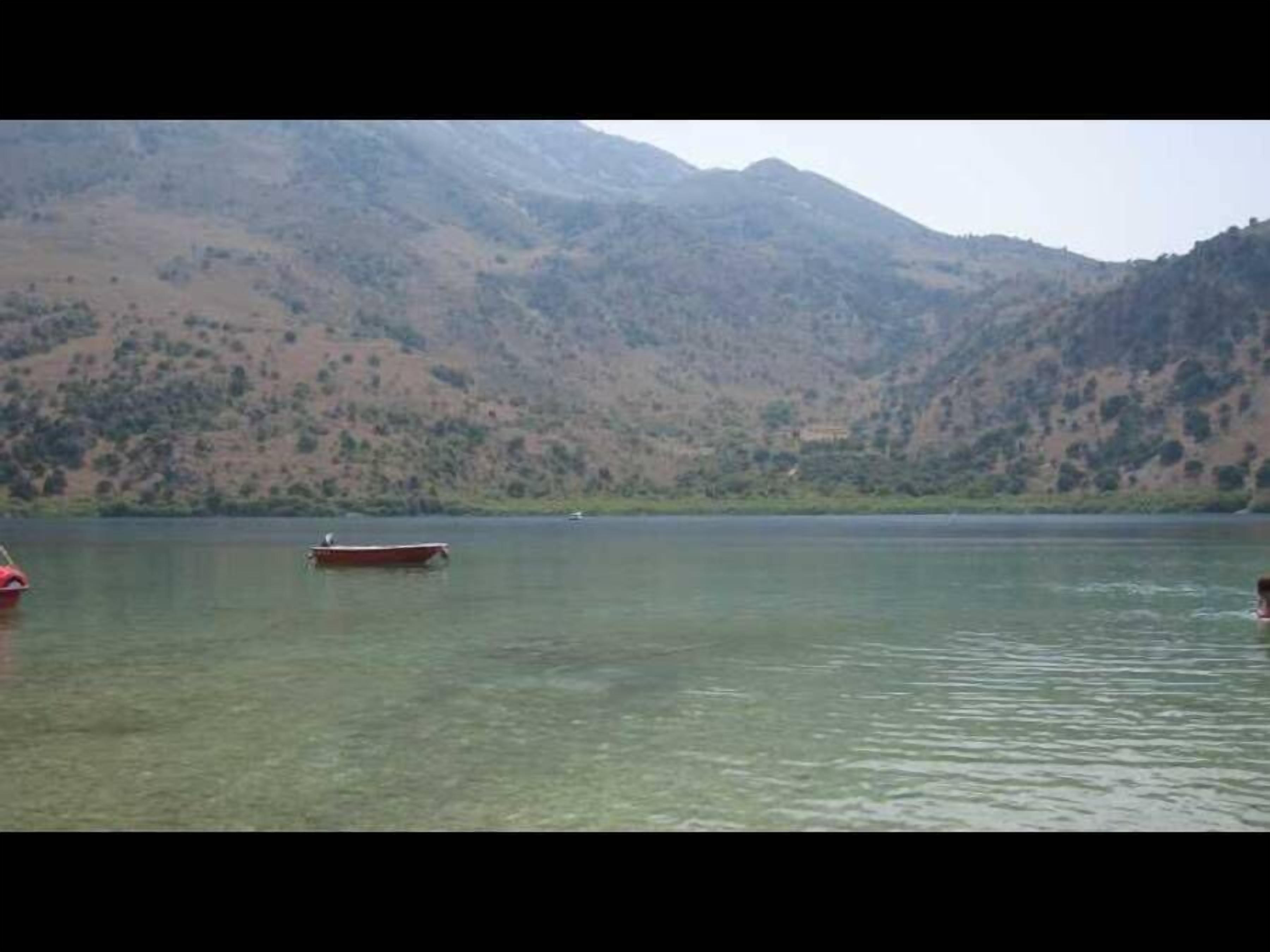 A calm lake with boats and mountains in the background.
